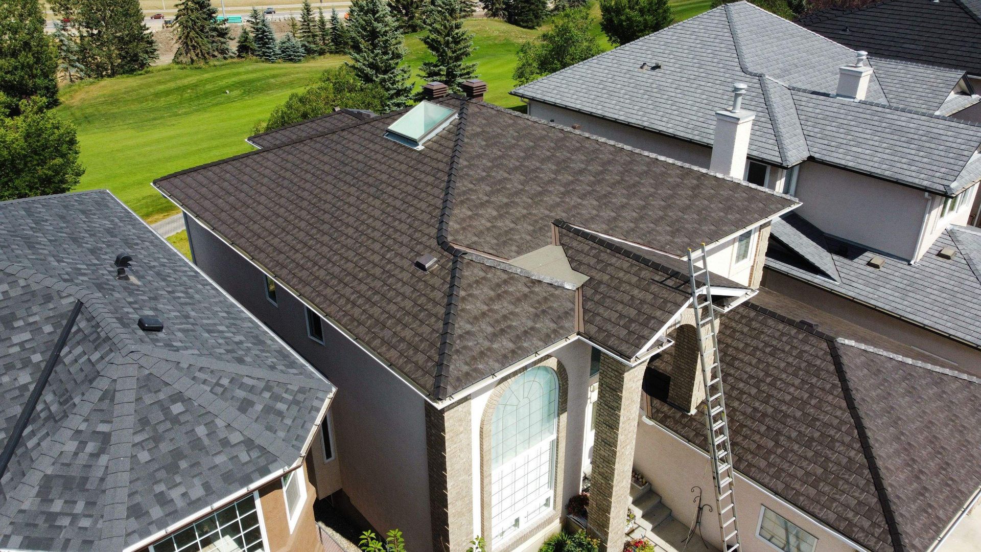 Aerial view of houses with brown and gray shingle roofs on sunny day.