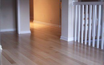 Hardwood floor, beige walls, white banister, hallway with natural light.