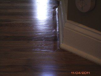 Dark wood floor with water damage near a white baseboard and a smoke detector.