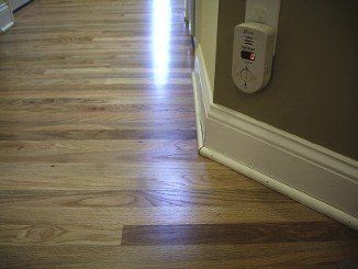 Wooden floor with a wall and baseboard; a carbon monoxide detector is mounted on the wall.