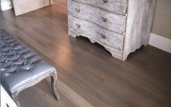 Bedroom with gray-toned wooden floor, tufted bench, and weathered chest of drawers.