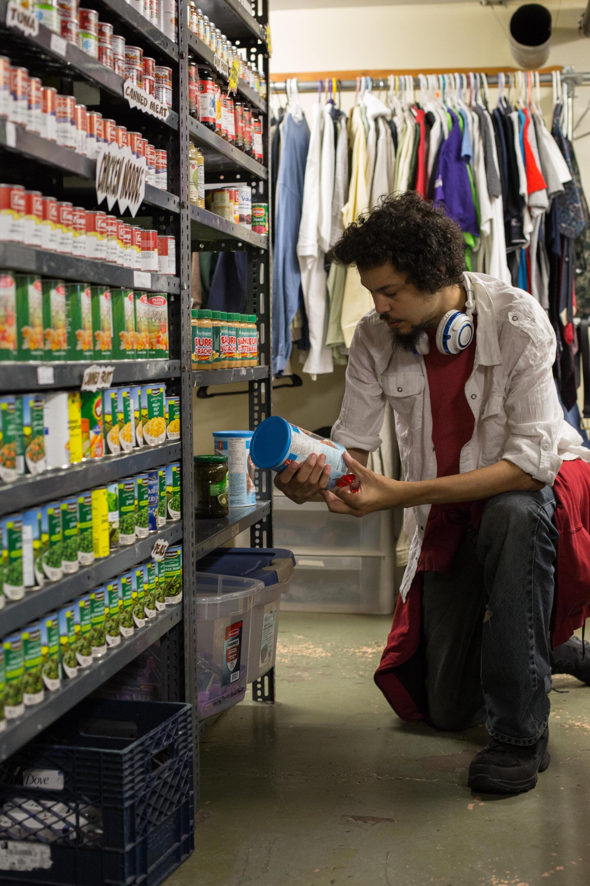 A man is kneeling down in a store looking at a can of food.
