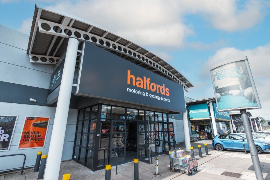 Halfords storefront with glass entrance, orange logo, and parked bicycles outside