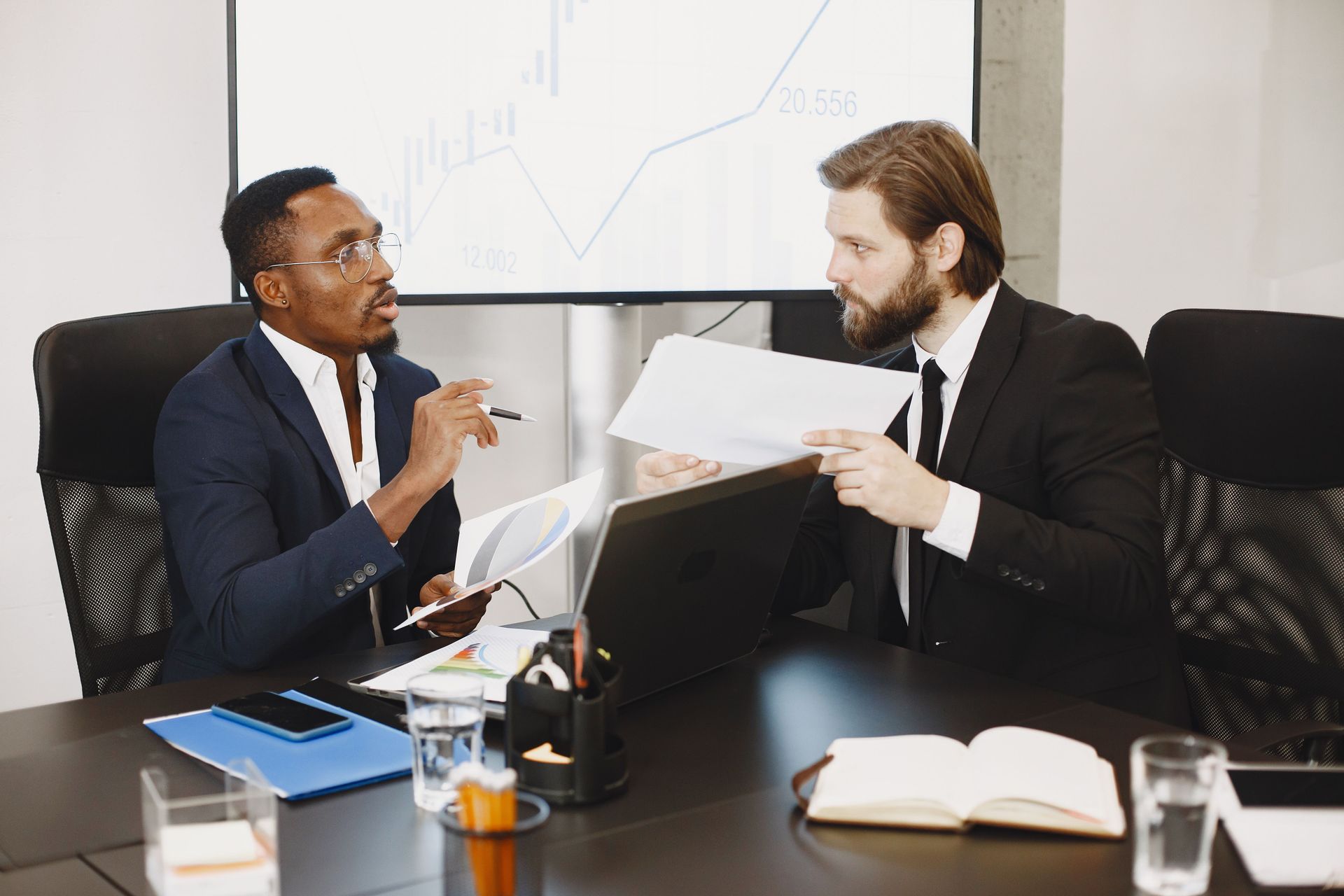 Two coworkers discussing documents across a desk in a conference room
