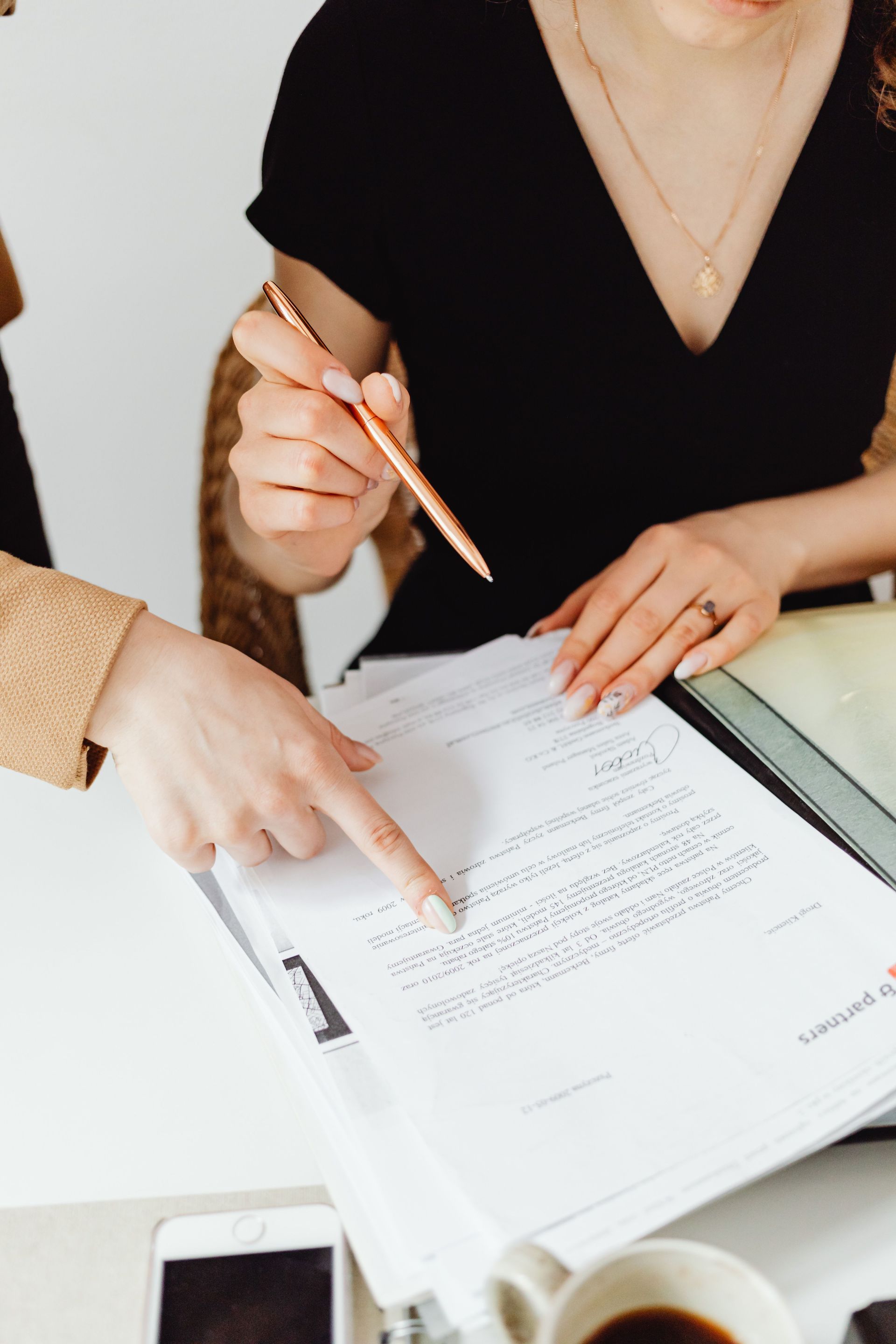 Two people review a document at a desk, one pointing while the other writes notes.