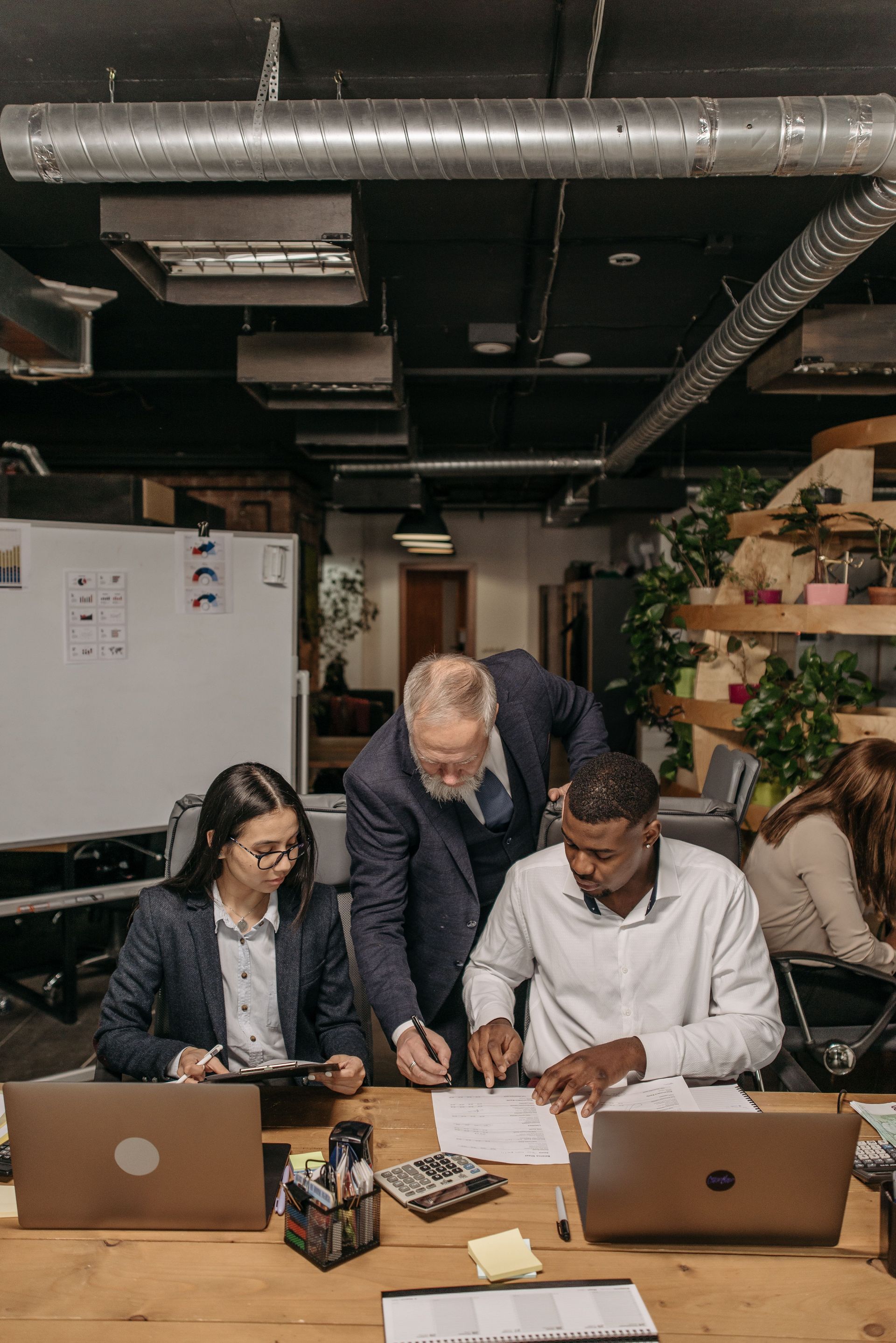 Colleagues reviewing documents at a shared office table with laptops, one person leaning over to help