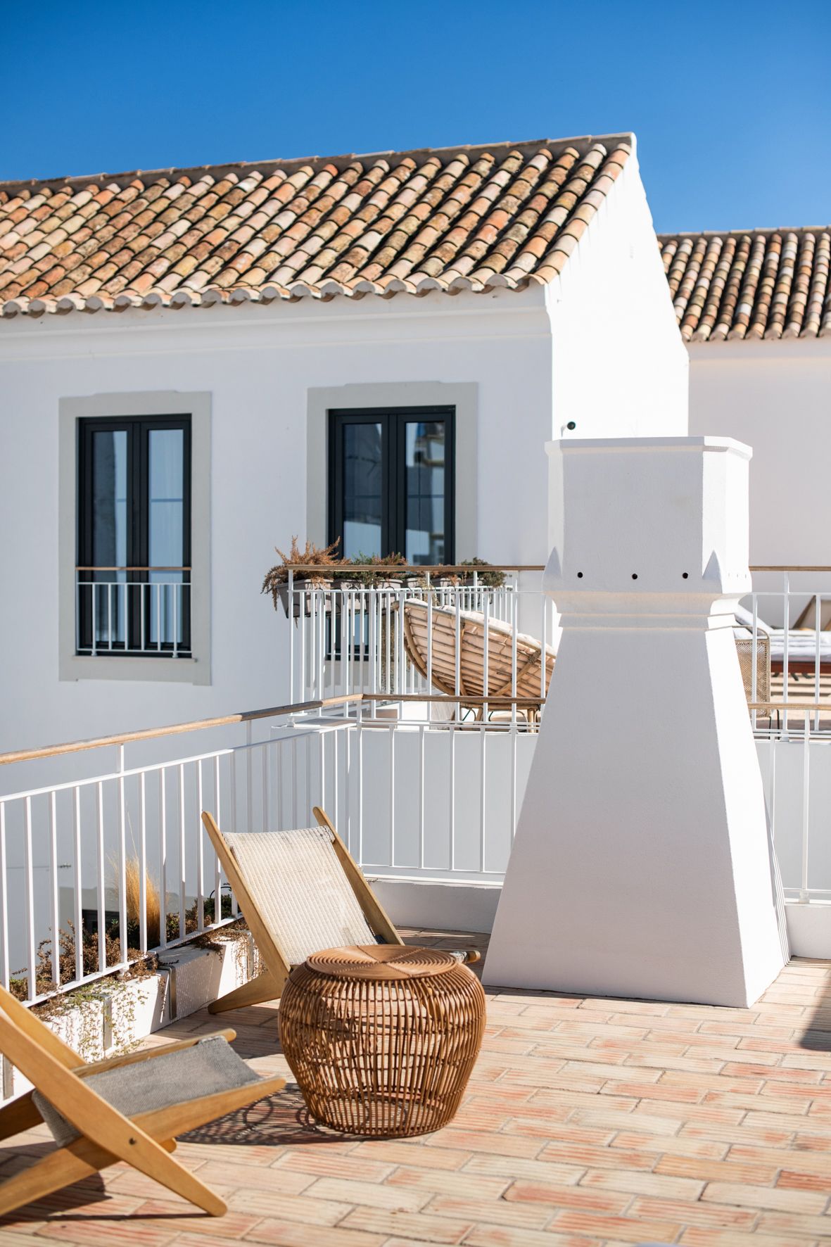 a white house with a brick roof and a balcony with chairs and a table .