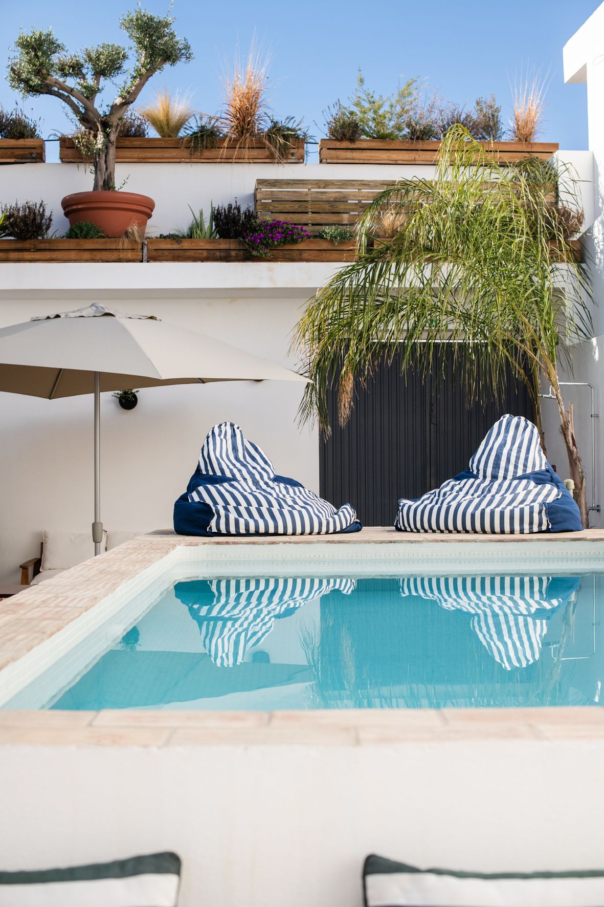 a swimming pool with two bean bag chairs and an umbrella in front of a building .