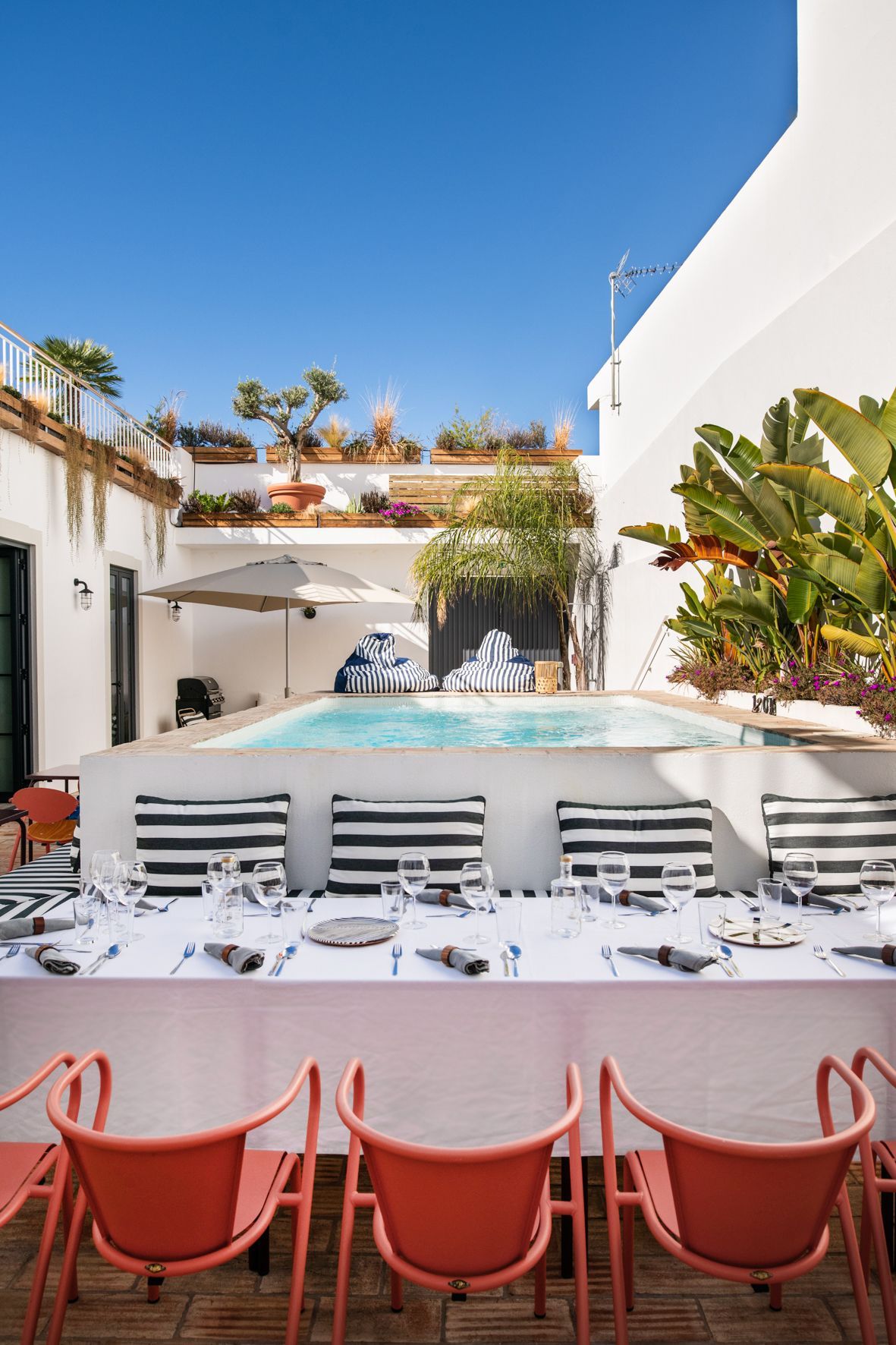 A long table with chairs and a pool in the background.