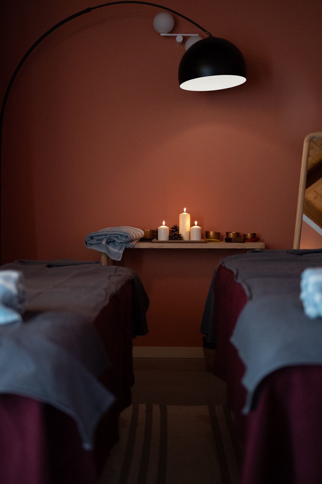 Massage room with two beds, red walls, shelf with candles, and a black lamp.