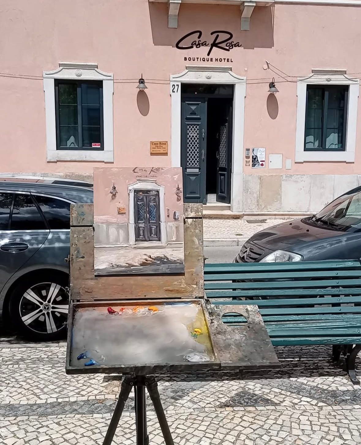 A painting on an easel in front of a building that says casa rosa