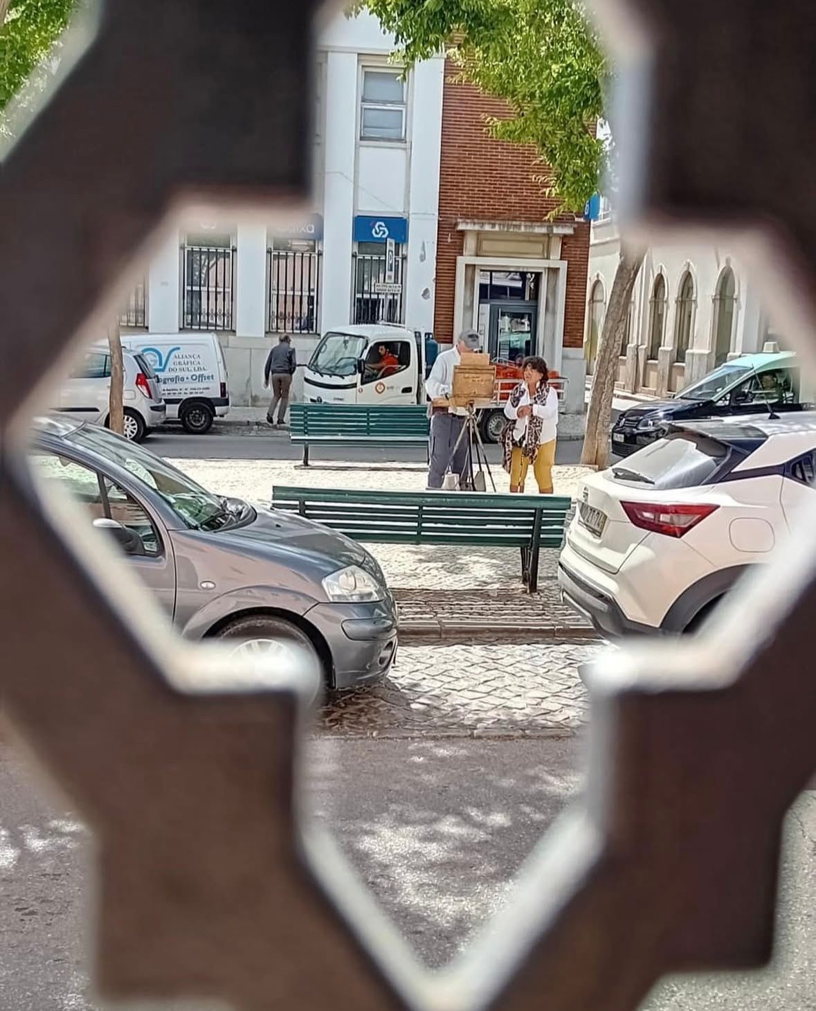 A view of a parking lot through a hole in a fence.