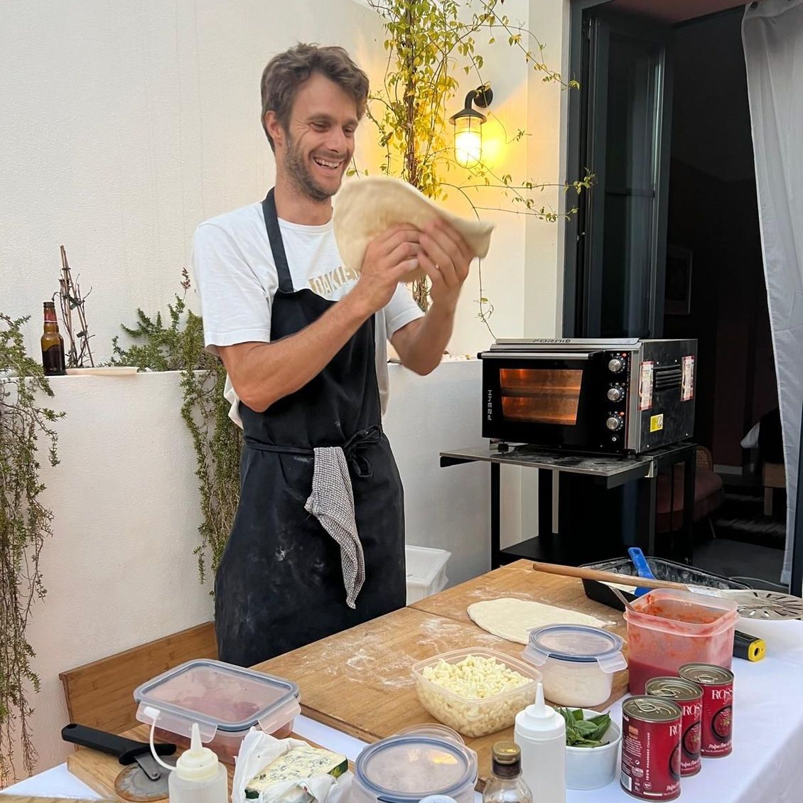 A man in an apron is holding a pizza dough in his hands