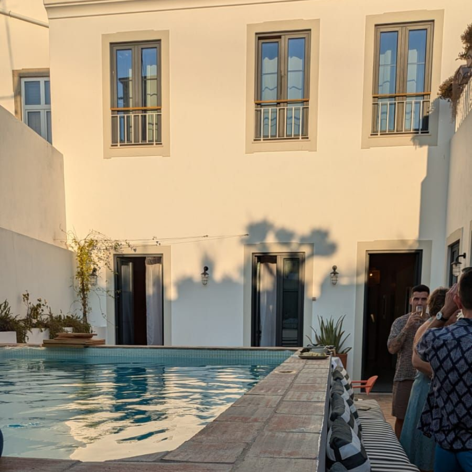 Courtyard with pool, white building, open doors, people, and sunlight.