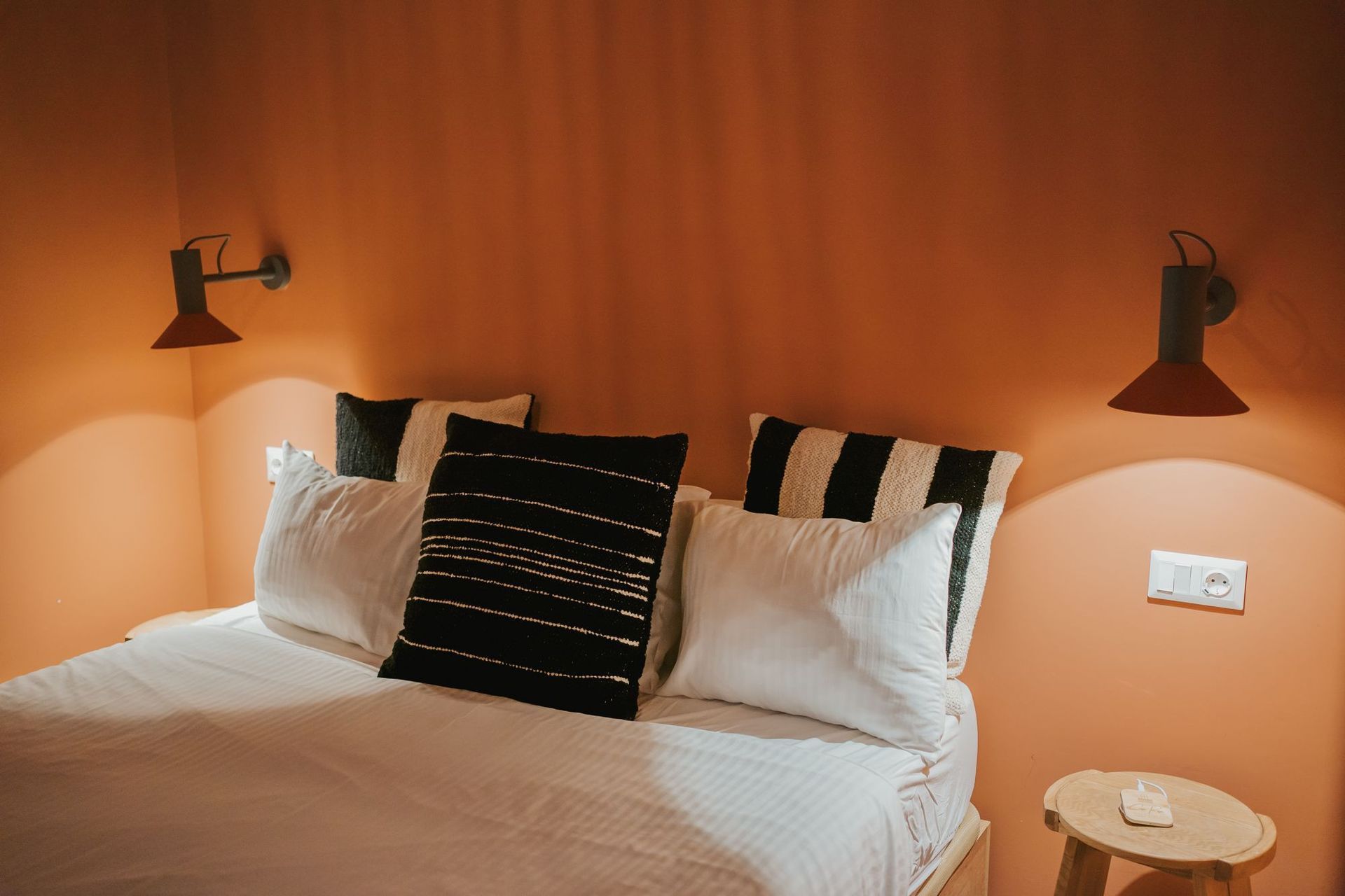Bedroom with orange walls, white bedding, black and white pillows, and red sconces.