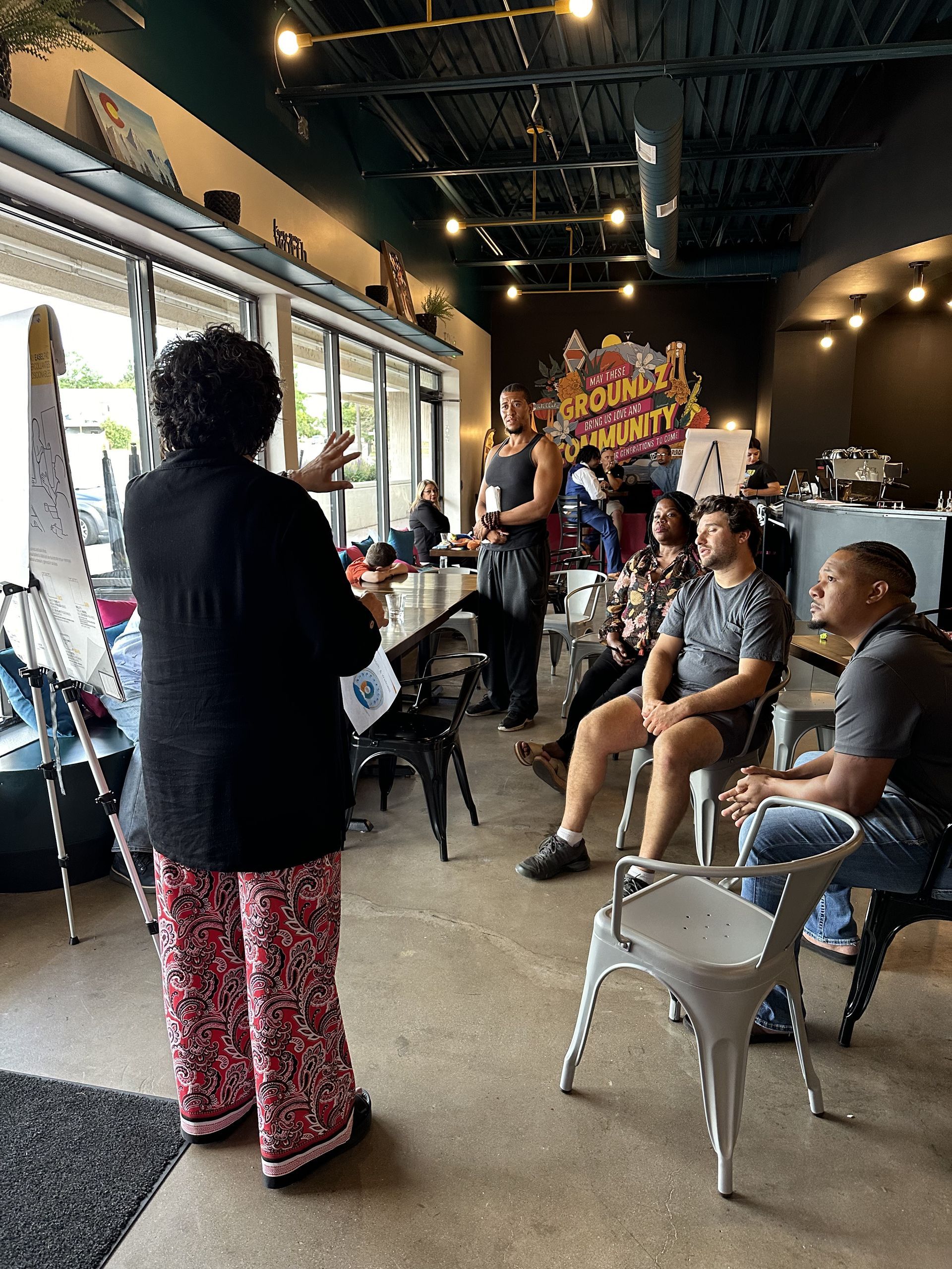 A woman is standing in front of a group of people sitting in chairs in a room.