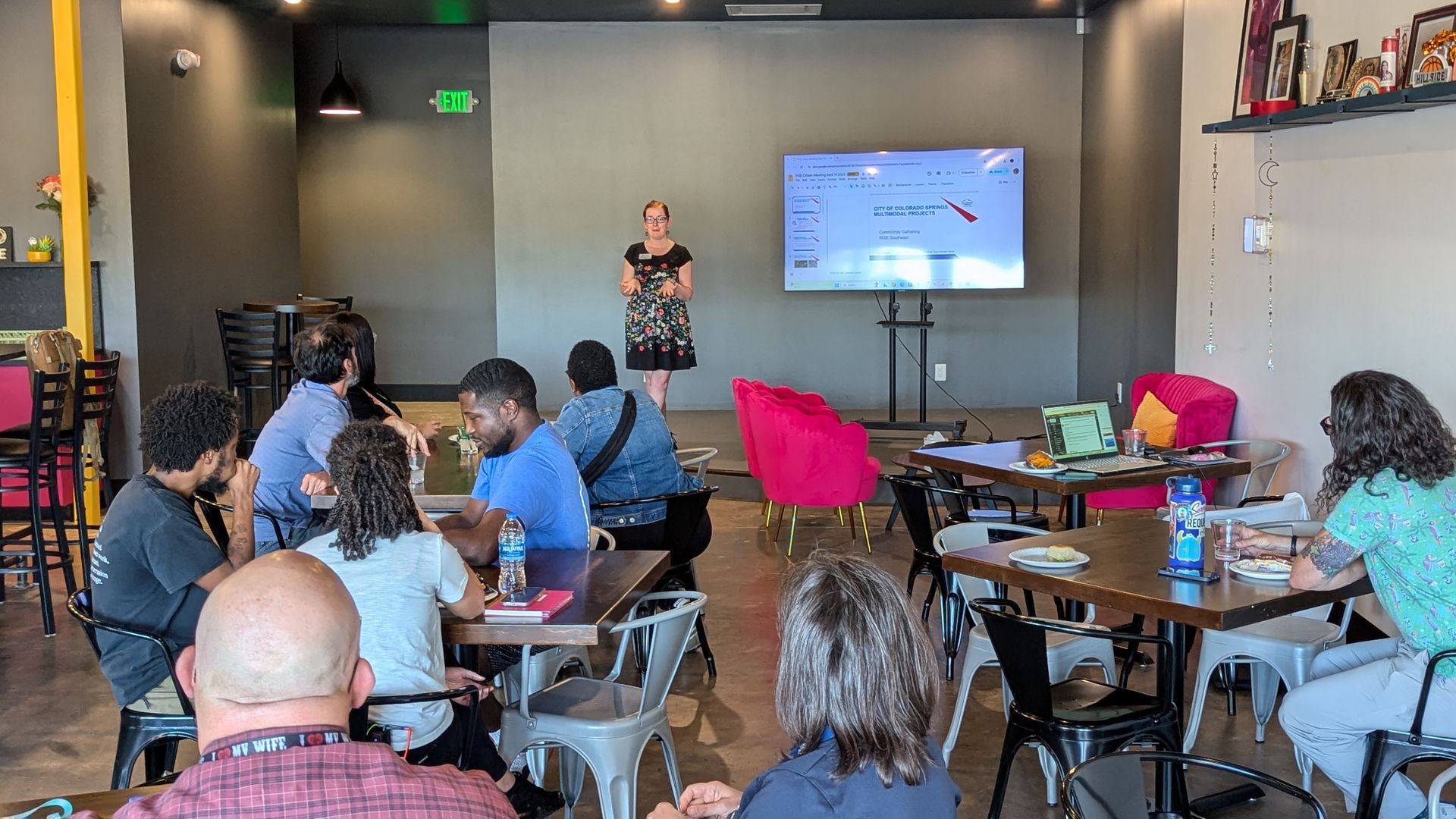 A woman is giving a presentation to a group of people sitting at tables in a restaurant.
