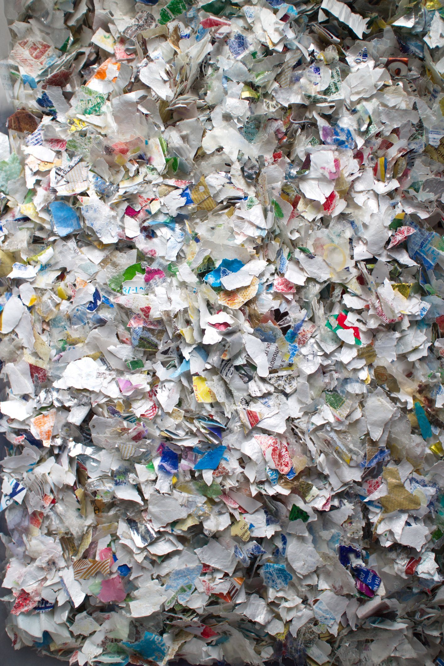 Shredded paper, mostly white, scattered on a wooden surface, revealing bits of colored print.
