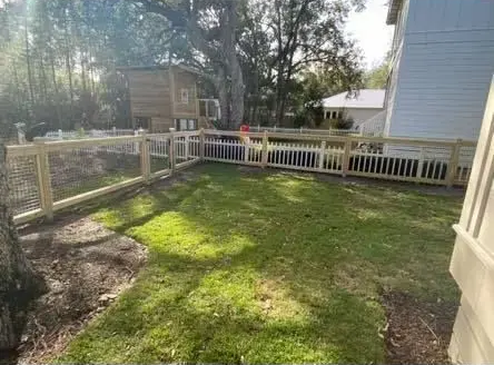 Sunny backyard with grass, patio pavers, fence, and a raised deck beside a house.