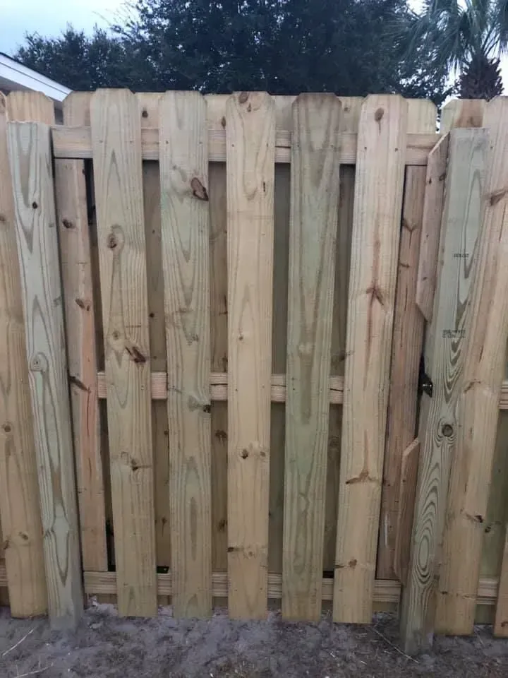A new wooden fence with vertical planks and metal hardware, set outdoors under cloudy sky.