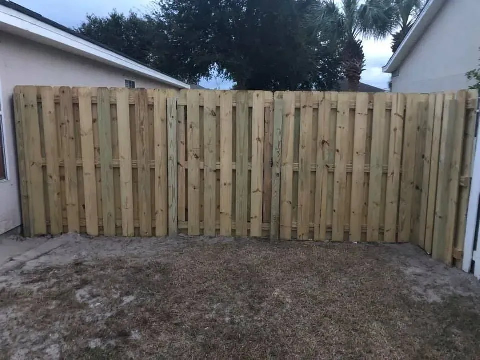 Fresh wooden privacy fence spanning between two buildings over a dirt yard.