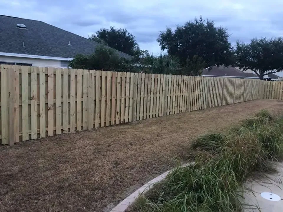 Long wooden privacy fence along a dry backyard with houses and trees in the background