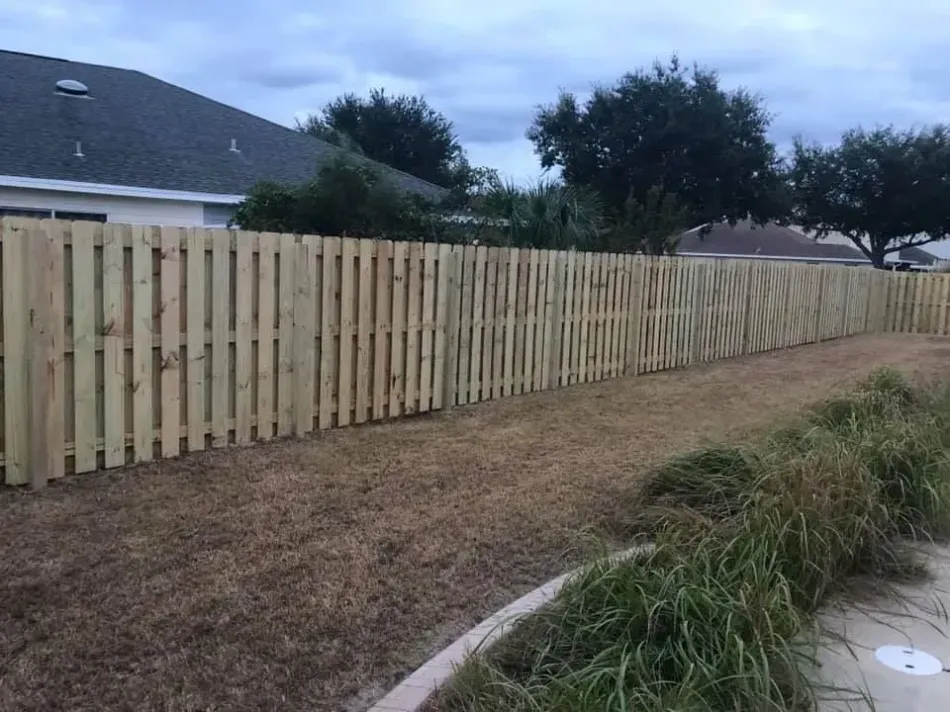 New wooden privacy fence along a grassy backyard beside houses at dusk