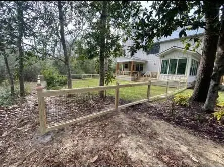 Wooded yard with a fence, trees, and a white house in the background