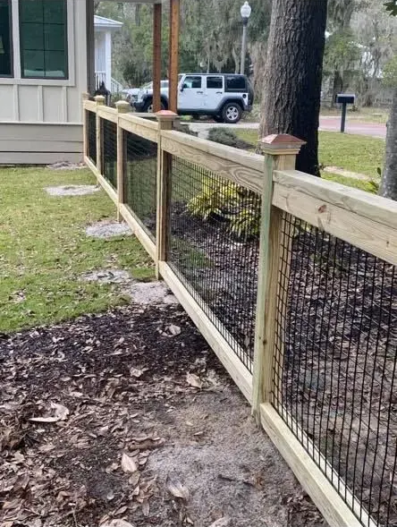 Wooden fence with wire mesh beside a house, with a black car parked in the background