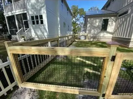 Backyard wooden gate and fence with grass, white house, and small shed on a sunny day