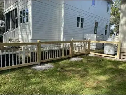 White house with porch and wooden fence beside a grassy yard in bright daylight