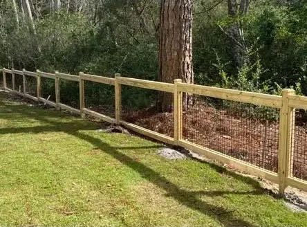 Wooden fence along a grassy yard with trees in the background under bright sunlight