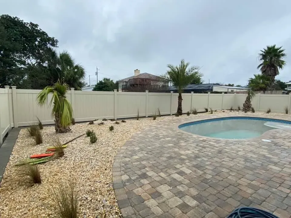 Backyard patio with a small pool, paver deck, gravel landscaping, and a beige privacy fence