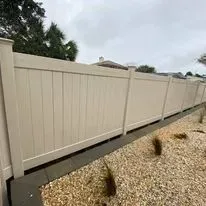 Beige vinyl privacy fence along a gravel yard on a cloudy day