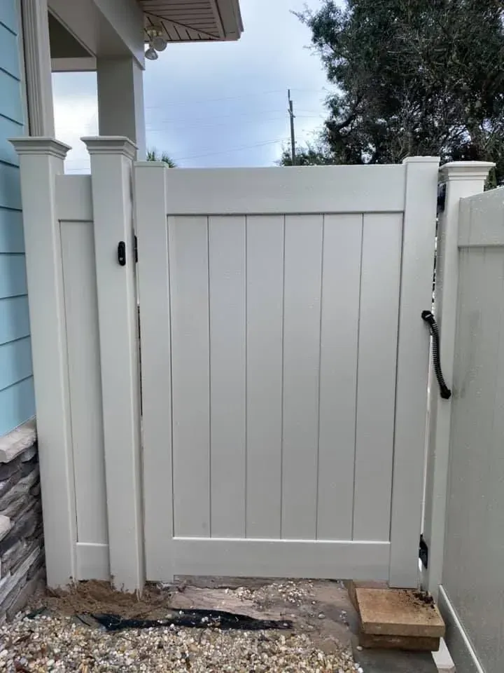 White vinyl gate between fence posts with black latch in a small outdoor yard area