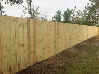 New wooden privacy fence along a dirt yard with trees in the background