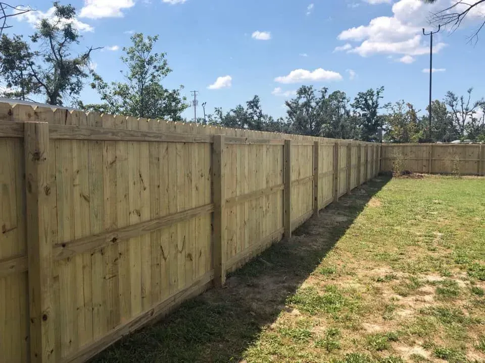 Wooden privacy fence along a grassy yard under a blue sky with clouds