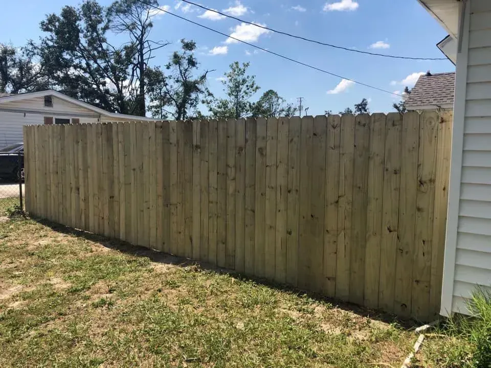 Wooden privacy fence along a grassy yard under a blue sky with power lines