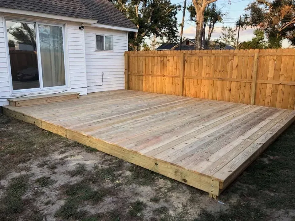 Wooden backyard deck beside a house, bordered by a tall privacy fence.