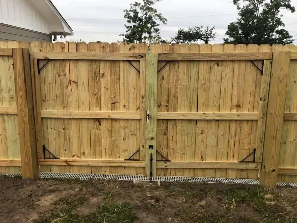 Wooden double gate in a fenced backyard with a house edge visible on the left.