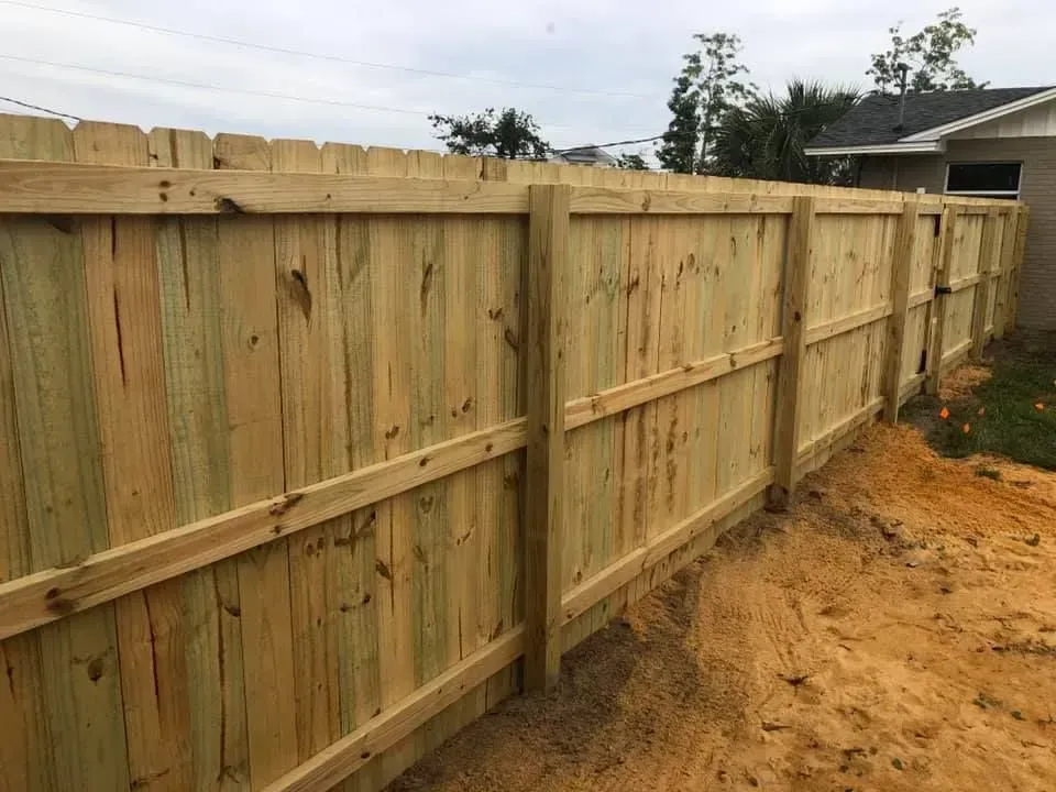 New wooden privacy fence along a sandy yard edge