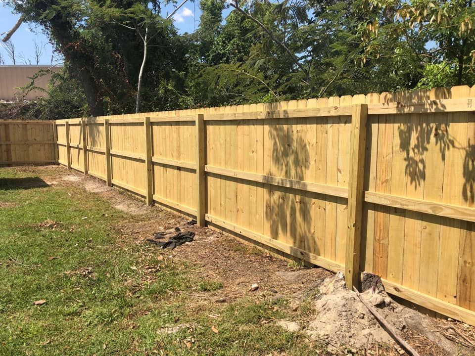 New wooden privacy fence along a grassy backyard with trees behind it