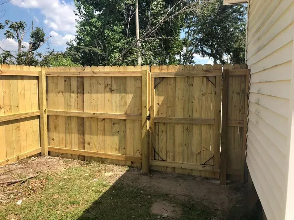Wooden backyard fence with gate beside a white house on a sunny day