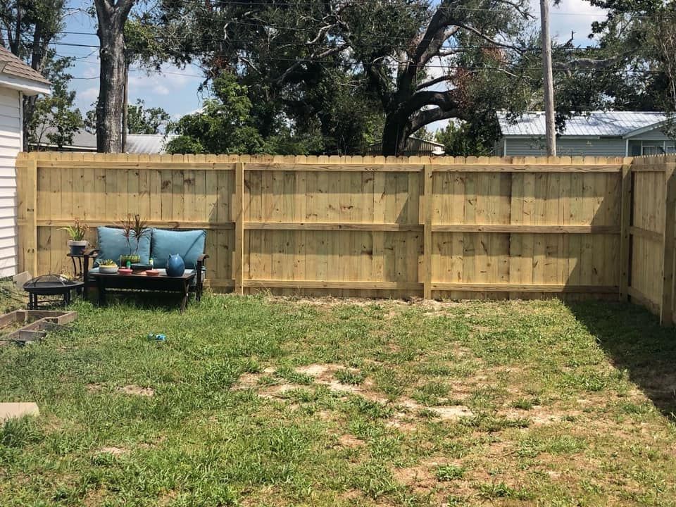 Backyard with a wooden privacy fence and a blue cart on the left, grass and trees in the background