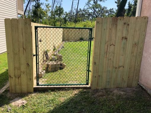 Wooden privacy fence with a green chain-link gate opening to a grassy backyard.