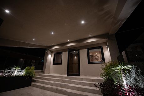 Ingresso della casa illuminato con scalini, faretti a incasso e giardino curato di notte
