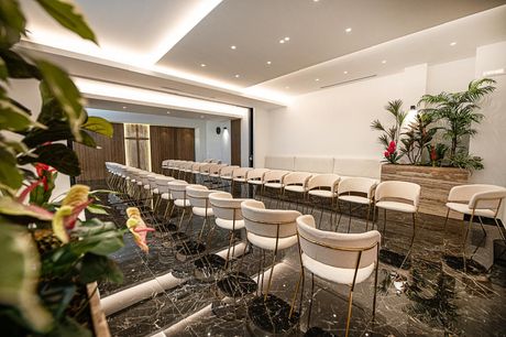 Sala conferenze moderna con file di sedie bianche, pavimento nero lucido e piante sotto faretti a incasso.