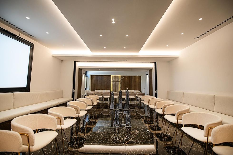 Sala conferenze moderna con sedie bianche, pavimento nero lucido e faretti a incasso a soffitto.