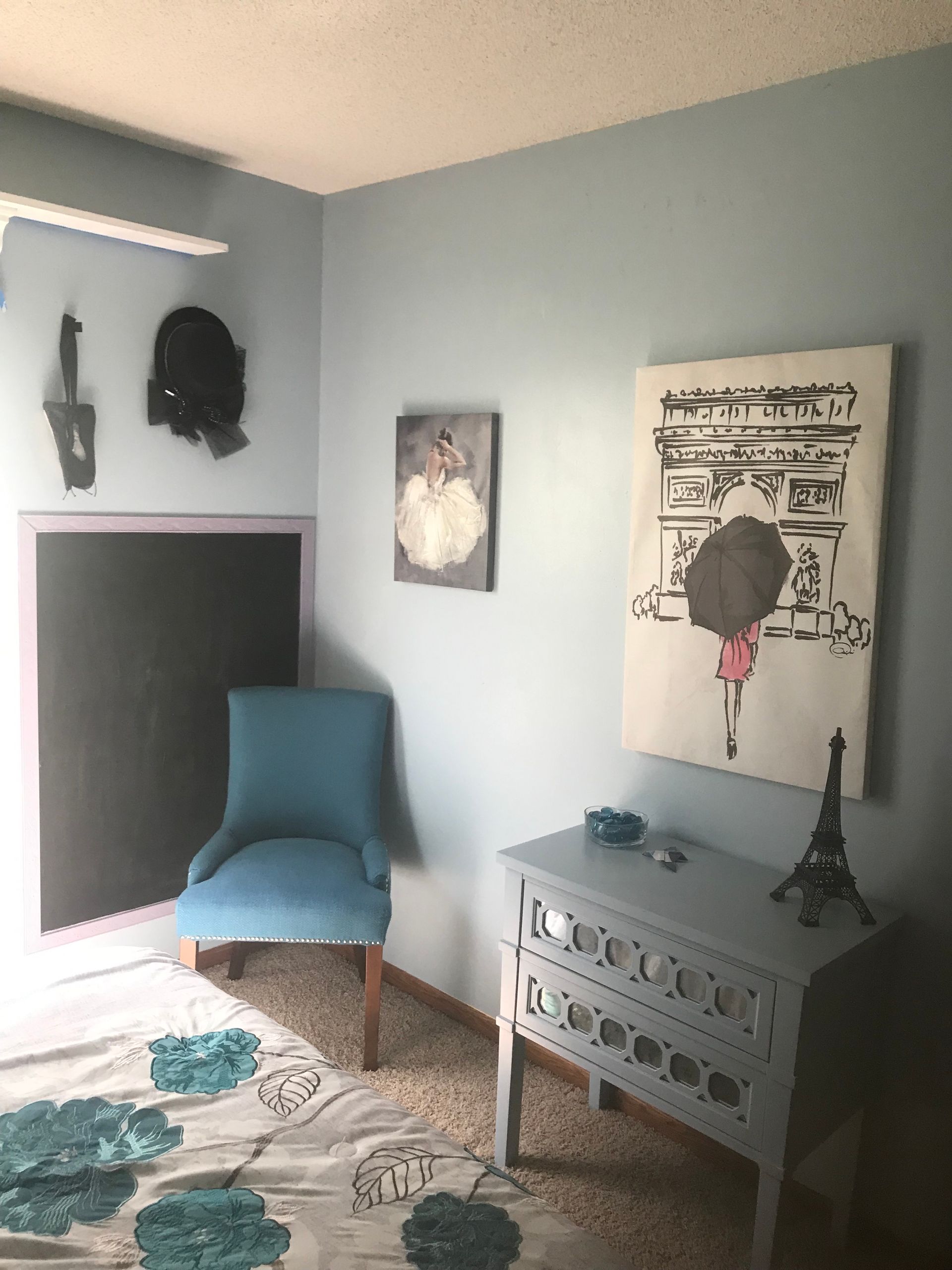 Bedroom corner: blue walls, art, chair, dresser, Eiffel Tower, and patterned bedding.