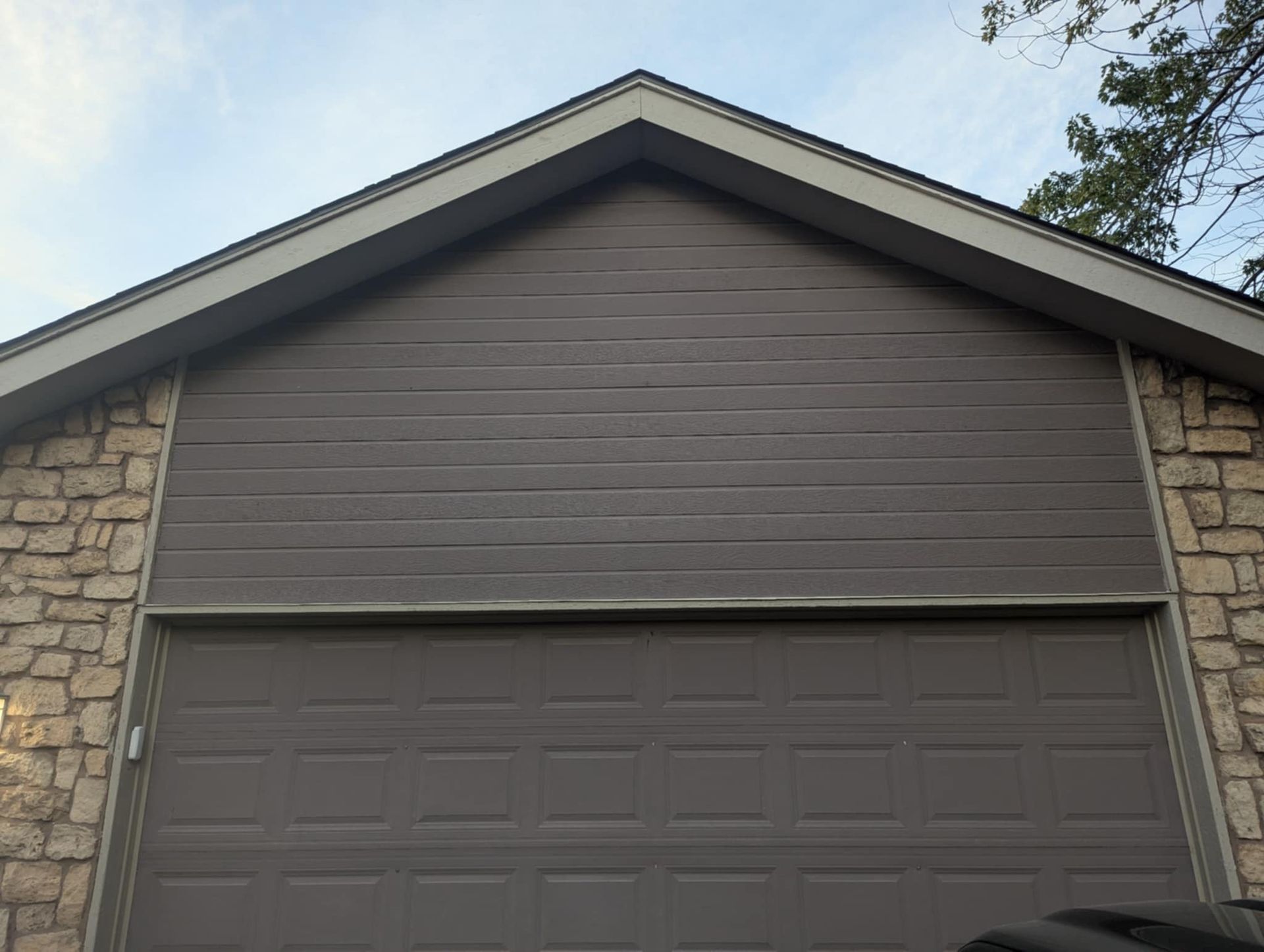 Brown garage door and siding, beige stone walls, under a beige trim roof.